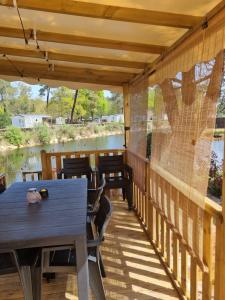 a covered deck with tables and chairs and a river at Mobil home camping Les ViVIERS Cap Ferret in Claouey
