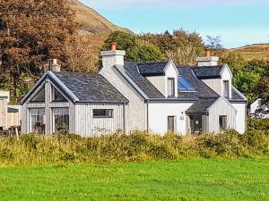 une maison blanche avec un toit noir dans un champ dans l'établissement Cuillin View, à Torrin