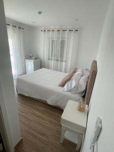 a white bedroom with a bed and a table at Alojamento Sudoeste in Zambujeira do Mar