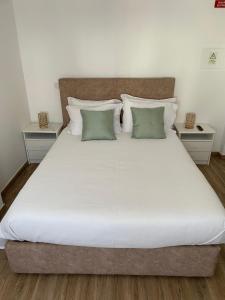 uma cama grande com lençóis brancos e almofadas verdes em Alojamento Sudoeste na Zambujeira do Mar