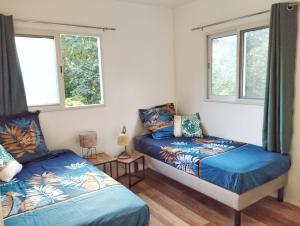 a bedroom with two beds and two windows at Kaz Kalina - Gîtes avec piscine partagée in Bouillante