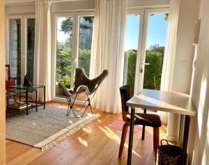 ein Wohnzimmer mit einem Stuhl, einem Tisch und Fenstern in der Unterkunft Quiet Studio with garden 8 Min from Beach in Estoril
