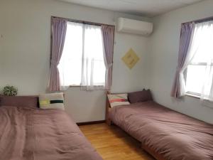 two beds in a room with two windows at ゲストハウス そよ旅 Guesthouse Soyotabi in Ishigaki Island