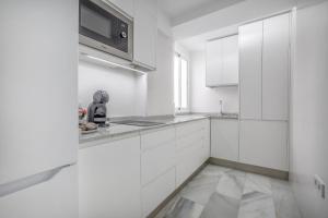 a white kitchen with white cabinets and a microwave at Apartamentos Haranas, parking incluido in Córdoba