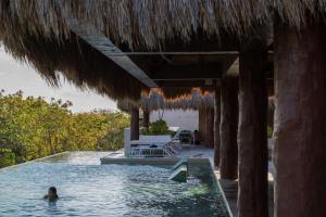a person in a swimming pool under a straw roof at Luxury & Modern Apartments in Tulum Top Amenities By Yeah in Tulum