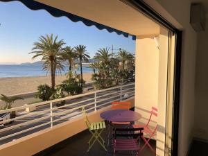 d'un balcon avec une table et des chaises et une vue sur la plage. dans l'établissement T2 Front de Mer 2pers 1 minute de la plageT2 de 44 m2 plus terrasse 16m2 , vue mer panoramique et en face de la plage Cet appartement refait à neuf bénéficie d'un confort et d un équipement optima Cet appartement est idéal pour 2 personnes avec sa chamb, au Lavandou