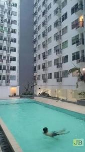 a person swimming in a swimming pool in front of tall buildings at Jarrdin Cihampelas C2218 in Bandung