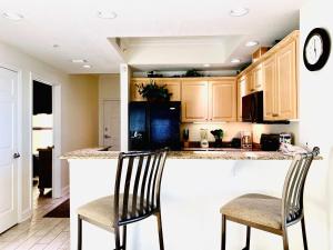 a kitchen with wooden cabinets and two chairs at a counter at Crystal Shores 1301 by ALBVR - Beautiful Beachfront Corner Condo with Gorgeous Views! in Gulf Shores