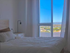 - une chambre avec un lit blanc et une grande fenêtre dans l'établissement Frente al mar, preciosas vistas, piscinas , valdelagrana, à El Puerto de Santa María
