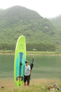 un hombre de pie junto a una tabla de surf y una paleta en Phong Nha A Little Leaf Homestay, en Phong Nha