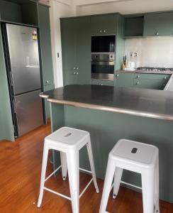 a kitchen with green cabinets and two white stools at CBD Apartment, River View in Hamilton