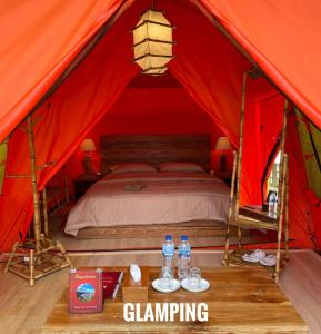 Kejajar的住宿－Bagas Luxury Camp，红色帐篷内的一张床位,桌子上装有水瓶