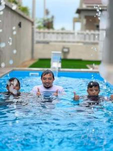 un hombre y dos niños nadando en una piscina en El Manzil Homestay with Pool en Guar Chempedak