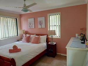 a bedroom with a bed with pink walls and two windows at Tingalpa Townhouse Treat in Brisbane