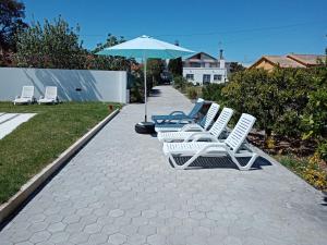 a row of white lawn chairs and an umbrella at Moradia Vila Rosa in Ponte de Vagos
