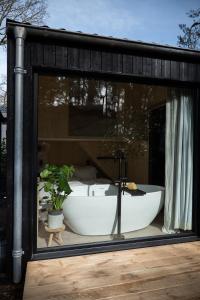 bañera en el interior de una ventana de cristal en Vague Luxurious Tiny House Luxe Wellness, Spa Bad,Beamer, Veluwe, en Nunspeet