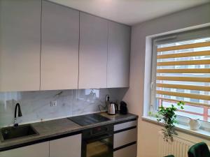 cocina con armarios blancos, fregadero y ventana en Apartament nr15 z parkingiem podziemnym, en Toruń