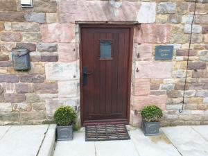a wooden door on a stone building with two plants at 2 Bed Chic Peak District Cottage Barn Near Alton Towers, Polar Bears, Chatsworth House in Leek