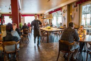 Een man die door een restaurant loopt met mensen aan tafel. bij Hotel De Spaenjerd in Kinrooi