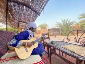 a woman sitting on a chair playing a guitar at Auberge la Palmeraie in Mhamid