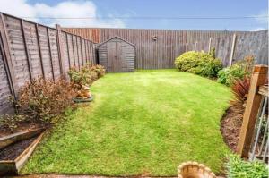 a backyard with a wooden fence and a green yard at Bulkington Lodge Coventry - Affordable Cosy Double & En-Suite Rooms in Bulkington