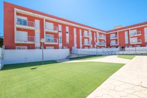 un bâtiment rouge avec une pelouse verte devant lui dans l'établissement Apartamento GELUM Delta del Ebro, à Sant Jaume d'Enveja