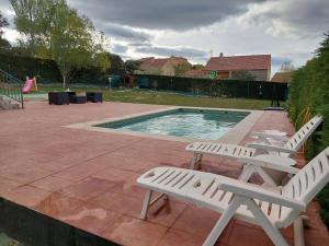- deux chaises blanches installées à côté de la piscine dans l'établissement Disfrutar y relajarse en el Robledal, à Zarzuela del Monte