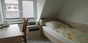 a small bedroom with a bed and a desk and two windows at Pension Lilli in Norddeich