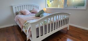 a white crib with pink and green pillows on it at Beach Cottage. 100m to the beach 9minutes to Hot Springs. Pet Friendly in Capel Sound