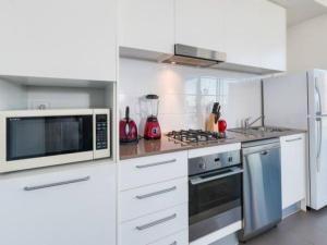 a white kitchen with a microwave and a stove at 806/67 Arvia in Newcastle