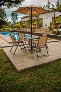 una mesa con sillas y una sombrilla junto a la piscina en Casa de Campo La Montaña en Tarija