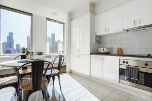 una cocina con armarios blancos y una mesa con sillas. en Urban Oasis on Collins en Melbourne