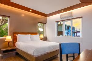 a bedroom with a bed and a desk and two windows at Amor Laut in Mabini