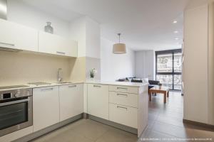 a white kitchen with white cabinets and a living room at Flateli Navas D02 in Barcelona