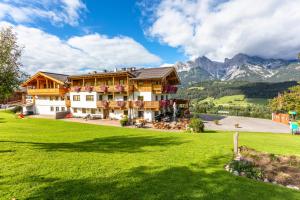 a large building on a green field with mountains at Berggasthof Hinterreit in Maria Alm am Steinernen Meer