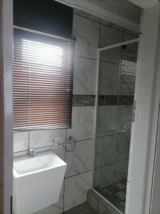 a bathroom with a sink and a glass shower at JM Gardens Guest House 