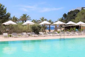 una piscina con sillas y sombrillas en un complejo en The Club Cala San Miguel Hotel Ibiza, Curio Collection by Hilton, Adults only en Puerto de San Miguel