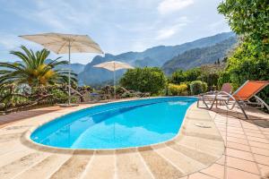 una piscina con sillas, sombrillas y montañas de fondo en Can Jaumins, en Sóller