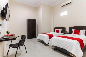 a bedroom with two beds and a desk and a television at RedDoorz At Ralica Grand Palladium Medan in Medan