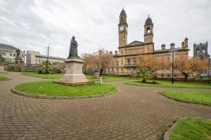 uma estátua em frente a um edifício com uma torre de relógio em Paisley Pad: Glasgow Gateway em Paisley