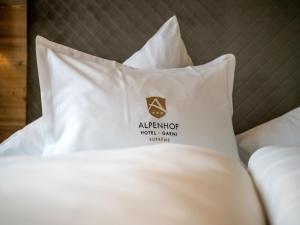 Una cama con sábanas blancas y una almohada con un cartel de hotel de apartamentos. en Alpenhof Hotel Garni Suprême, en Zell am Ziller
