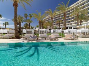 a pool with chairs and palm trees and a building at Paradisus Gran Canaria in San Agustin