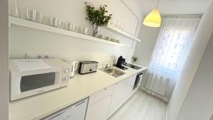 eine weiße Küche mit Mikrowelle und Spüle in der Unterkunft Eliza Apartman Veszprém in Veszprém