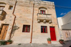 a brick building with a red door and windows at Stunning 3 bedroom Farmhouse with pool in Xagħra