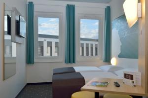 a room with a bed and a table and windows at B&B Hotel Halle (Saale) in Halle an der Saale