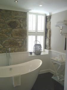 a bathroom with a tub and a stone wall at Headland House Luxury B&B in St Ives
