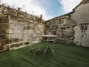 a table and chairs in a yard with a stone wall at Rose Cottage in Whitby