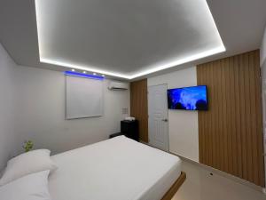 a bedroom with a white bed and a tv on a wall at Alegria Hostal in Santiago de los Caballeros