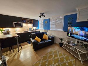 a living room with a black couch and a kitchen at Hayling Hideaway, private cosy annex near to beach in South Hayling