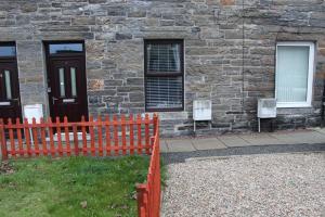 a red fence in front of a stone building at Newly Refurbished 2 Bedroom flat on NC500 route in Wick
